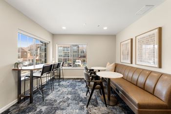 A room with a brown leather couch, a table with chairs, and two framed pictures on the wall.