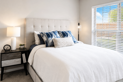A bedroom with a white bed and a nightstand with a lamp.