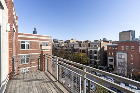 A balcony with a metal railing overlooks a parking lot and buildings.