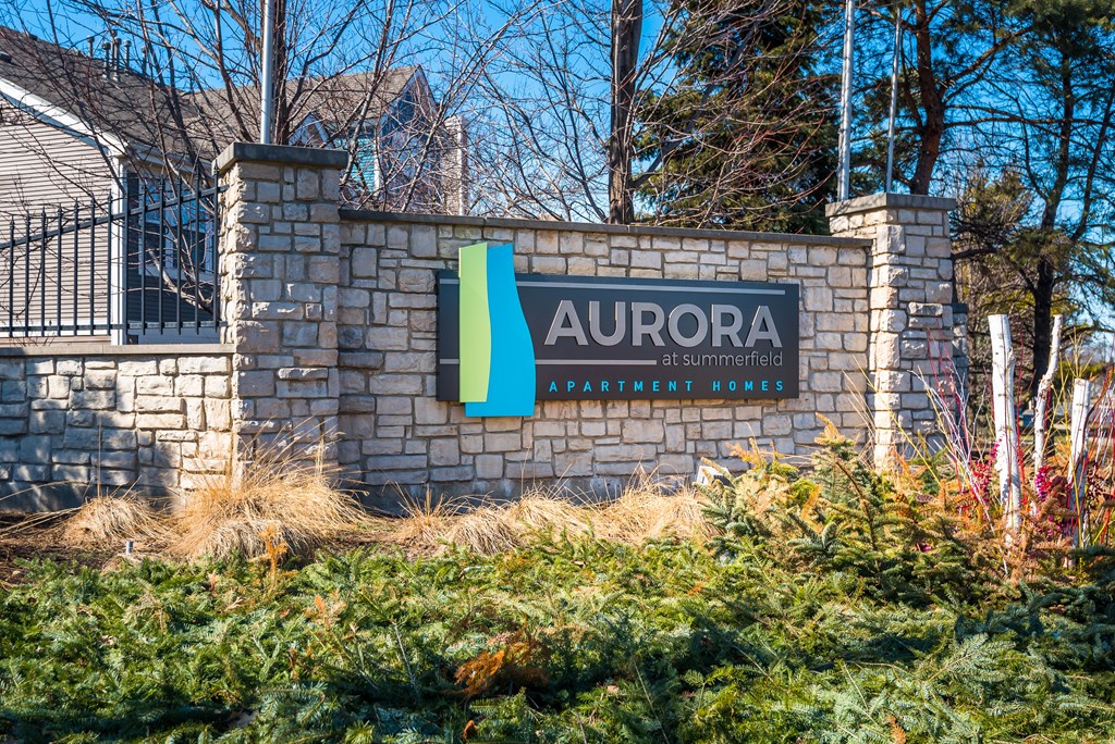 A sign for Aurora at Summerfield Apartment Homes is displayed in front of a house.