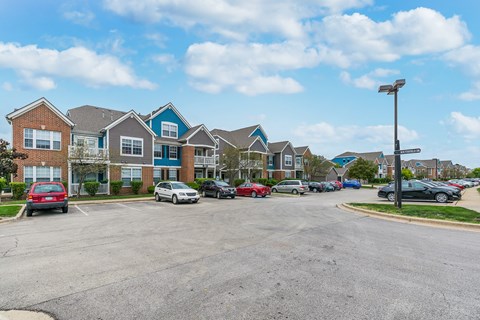 A parking lot with cars and a street sign in front of a row of houses.