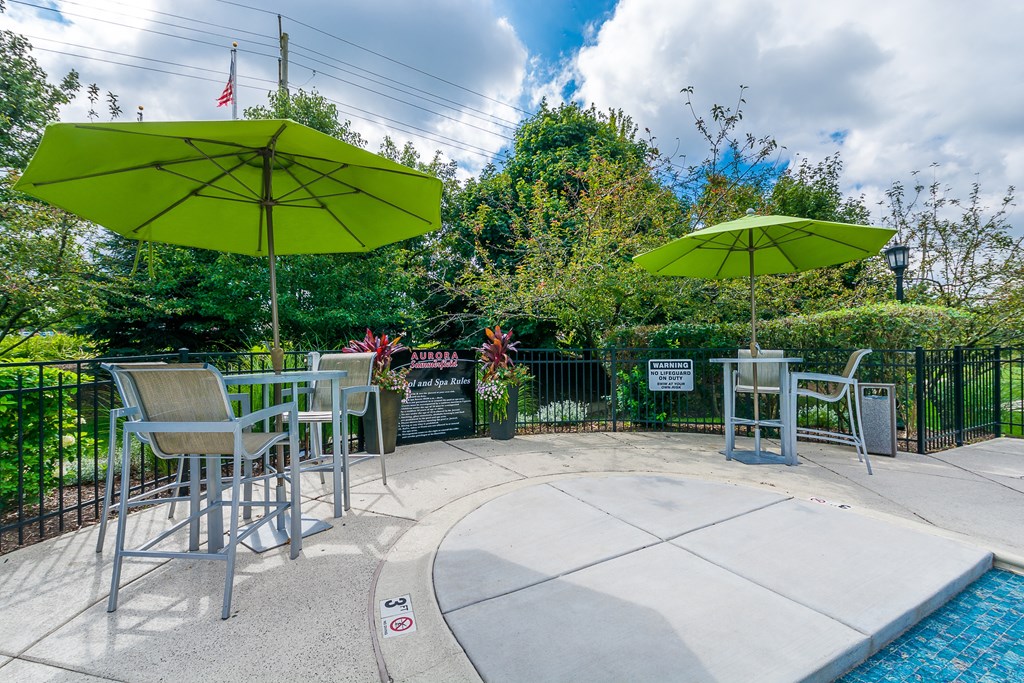 A pool area with a table and chairs under umbrellas.