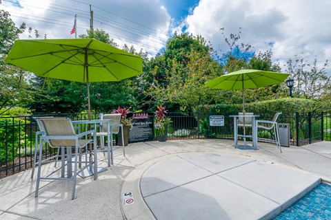 A pool area with a table and chairs under umbrellas.