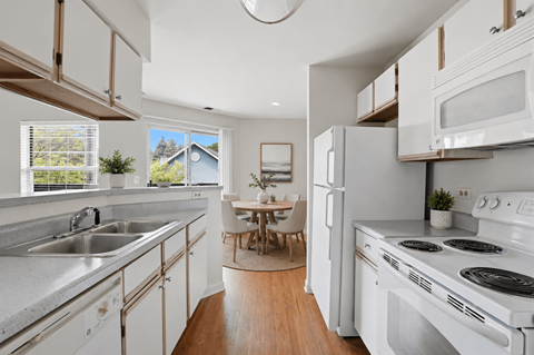 A modern kitchen with white appliances and wooden floors.