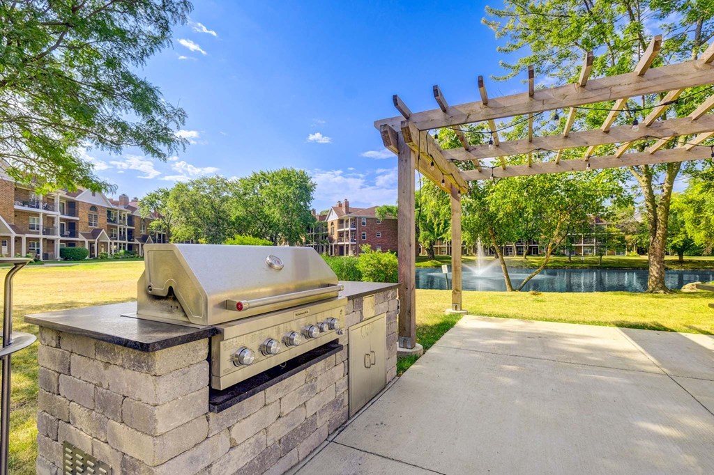 A BBQ grill is on a stone base in a sunny park.
