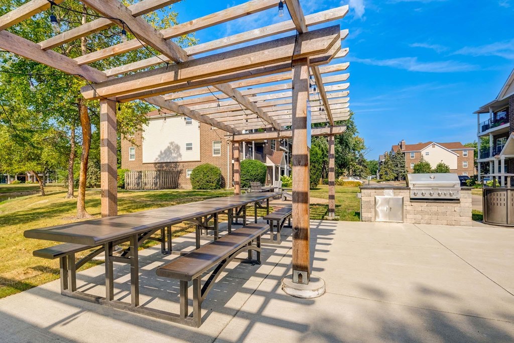 A wooden pergola with benches is situated in a sunny outdoor area.