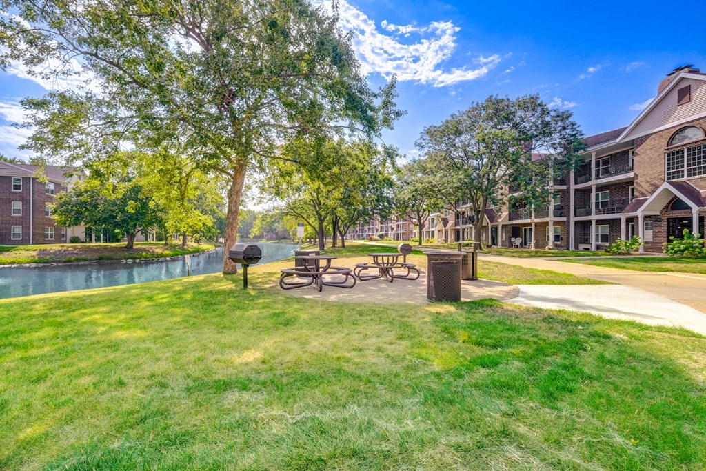 A park area with a bench and a tree in front of apartment buildings.