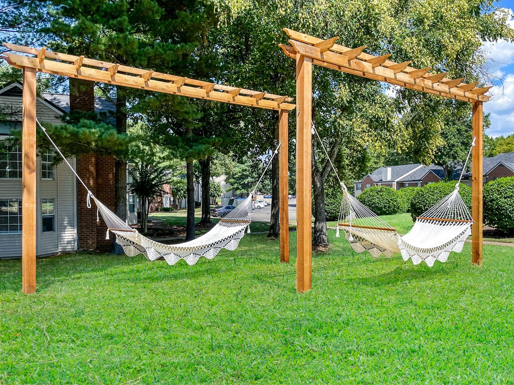 a pair of hammocks in the grass under a wooden structure