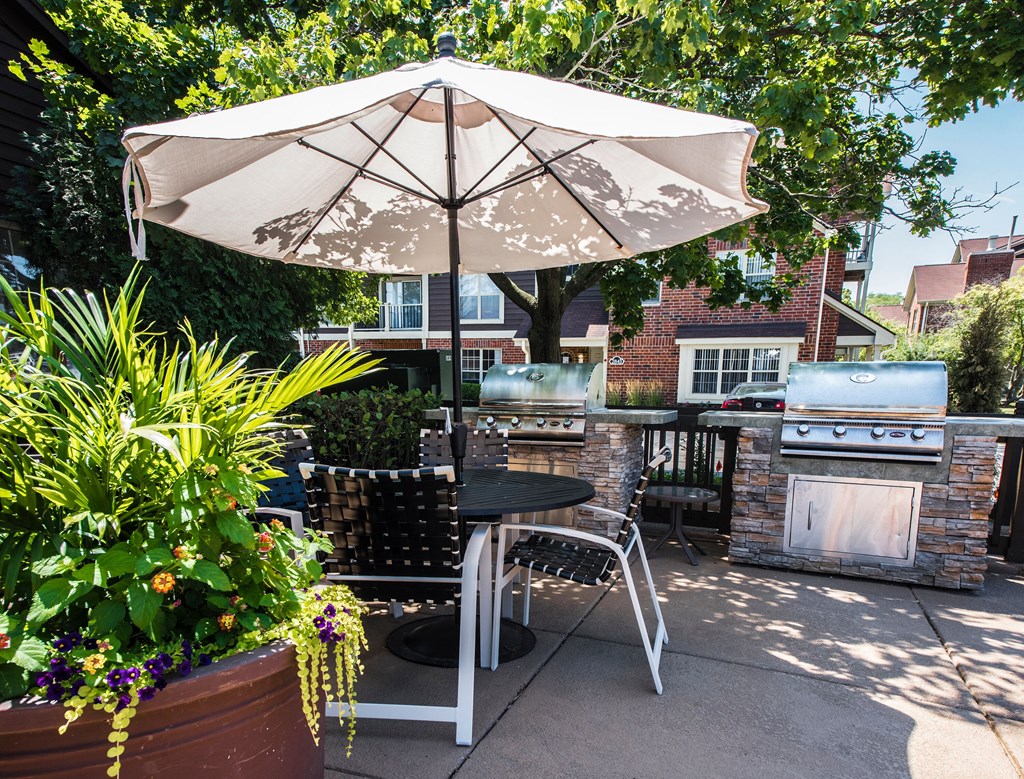a patio with an umbrella and a table with chairs and a grill