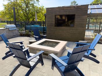 A fire pit is surrounded by blue chairs in a backyard setting.