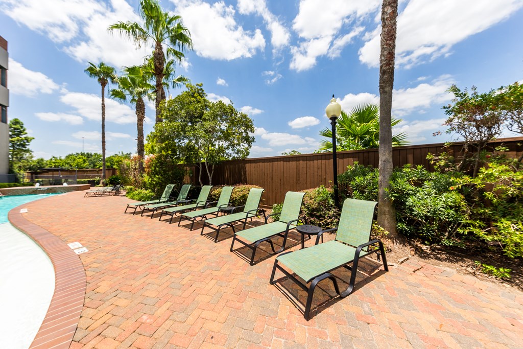 a group of lounge chairs on a brick patio next to a pool