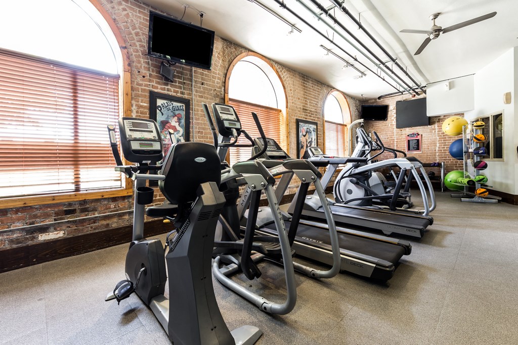 a gym with cardio equipment and weights in a building with brick walls