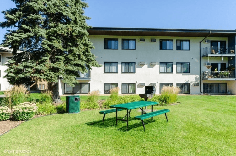 an apartment building with a green picnic table in the grass