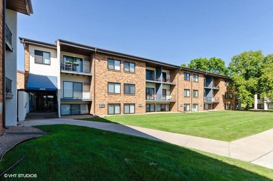 an apartment building with a green lawn and a sidewalk