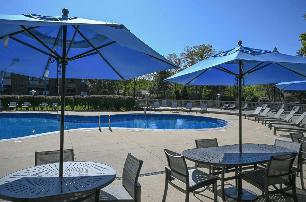 a swimming pool with blue umbrellas and tables with chairs