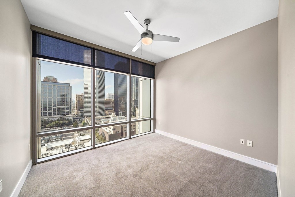 an empty living room with a large window and a ceiling fan