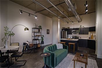 A living room with a green couch and a kitchen in the background.