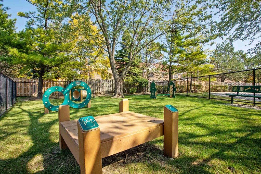 A wooden bench with a green trash can next to it in a park.