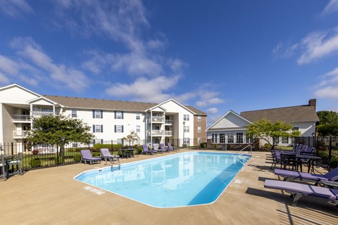 A swimming pool surrounded by lounge chairs and apartment buildings.
