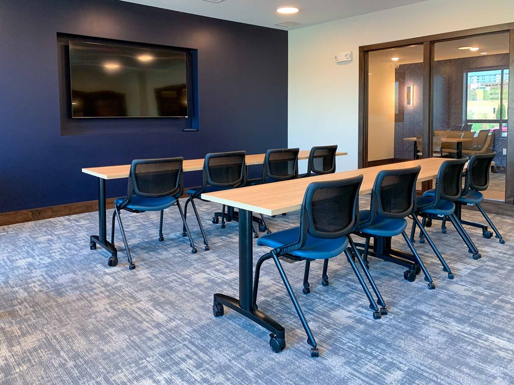 A conference room with large tables and chairs facing a presenting TV