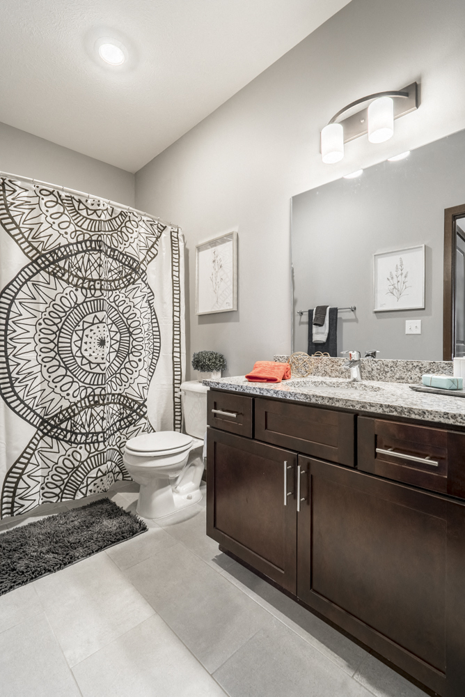 Bathroom with dark cabinetry and light granite countertops at 360 at Jordan West best new apartments West Des Moines IA 50266