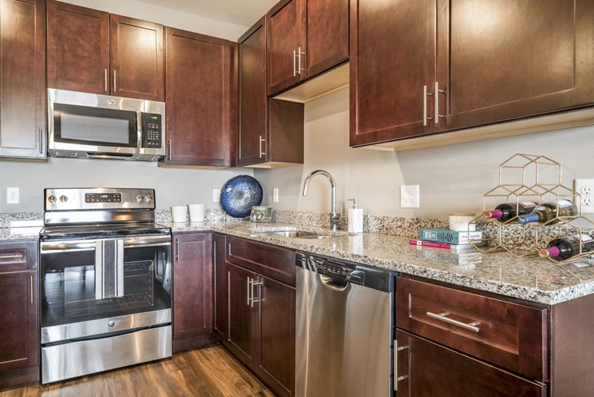 Kitchen featuring light granite countertops, dark cabinetry and stainless-steel appliances at 360 at Jordan West best new apartments West Des Moines IA 50266