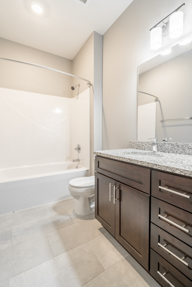 Bathroom with shower and tub, dark cabinetry and light granite countertops at 360 at Jordan West best new apartments West Des Moines IA 50266