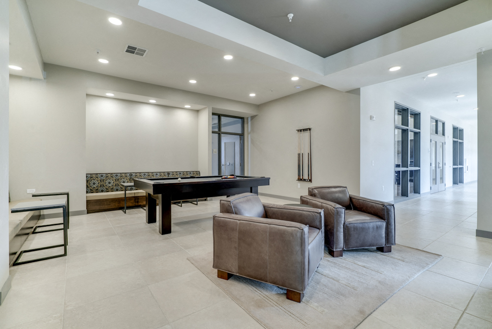 Game room in Ascend at Woodbury apartments' clubhouse with pool table and leather chairs.