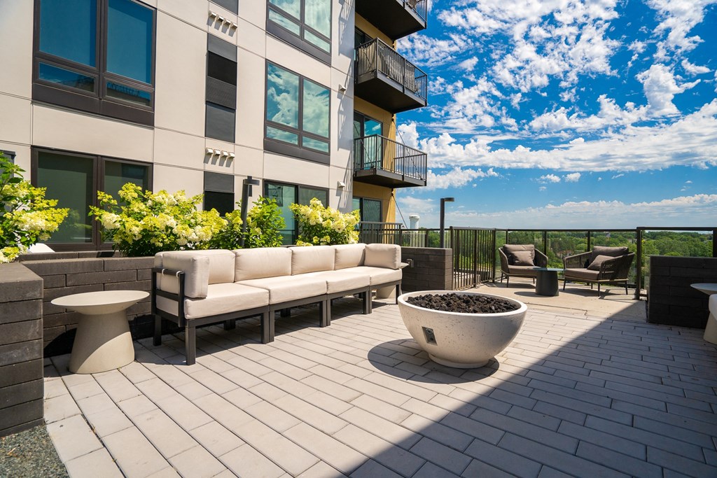 Outdoor lounging area with beige couch, a couple chairs, and fire place.