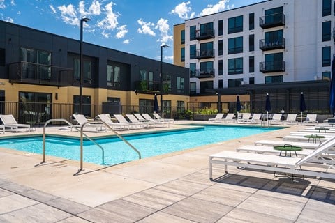 Resort style swimming pool with white sun loungers and green circular side tables at Aspire at CityPlace