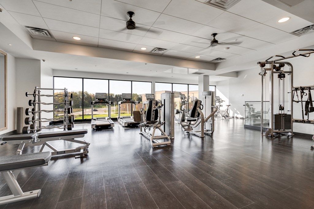 Fitness center with full-wall windows and dark brown wood floors in luxury apartment