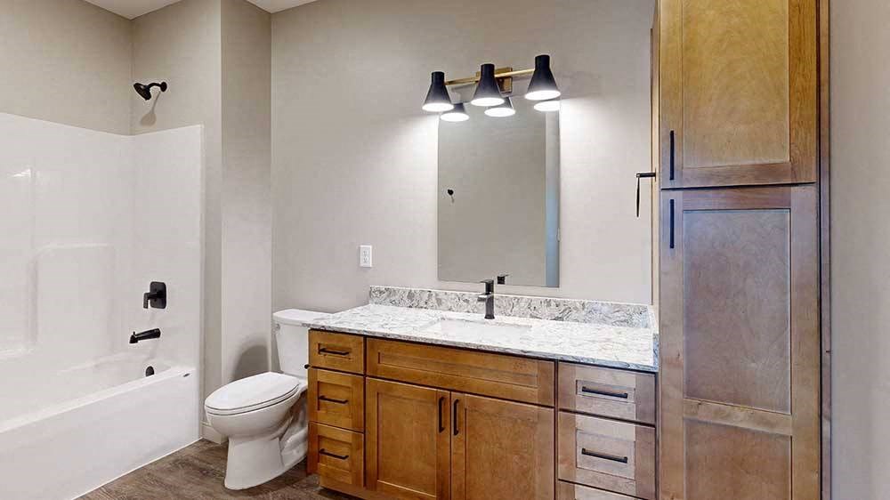 a bathroom with a light brown cabinets, a tall storage cabinet, quartz vanity sink, a mirror, and a shower and tub