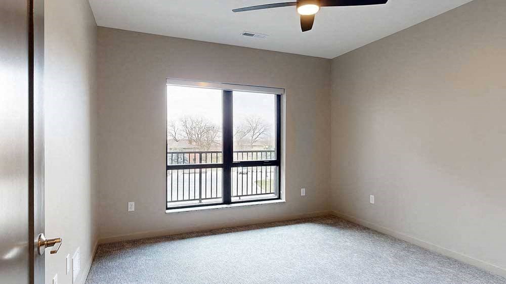 a bedroom with a ceiling fan and a large window overlooking a balcony