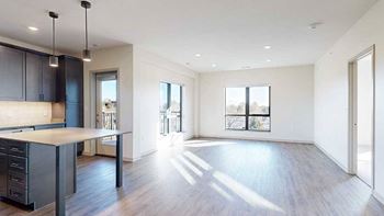 a spacious living room with large windows and a modern kitchen with dark wooden cabinets