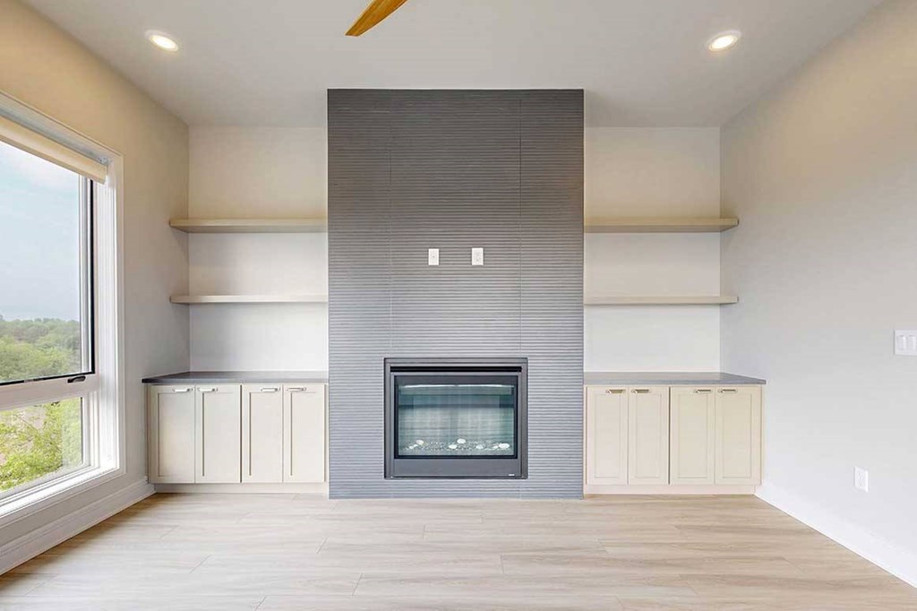 A modern living room with a fire place in a floor-to-ceiling mantel, and built-in cabinetry and shelves on either side.
