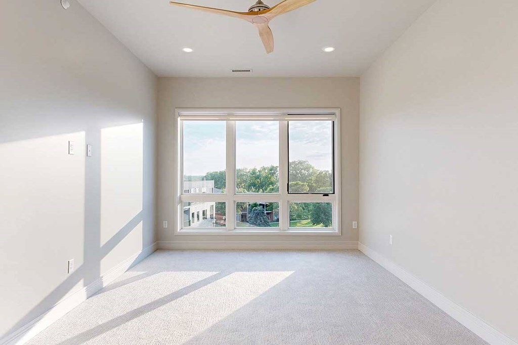 A carpeted bedroom with a floor-to-ceiling 3-panel window, and a ceiling fan.