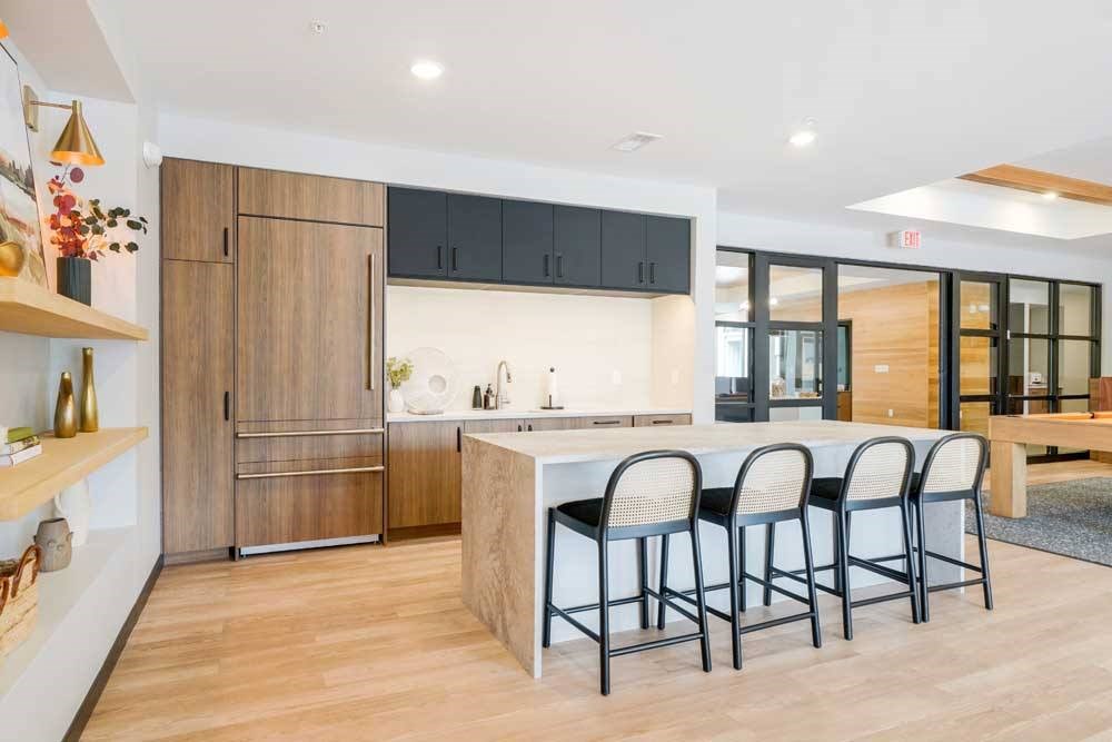 A kitchen in the clubroom with a faux wood fridge, white quartz countertops, and a large island with rattan-back bar stools.
