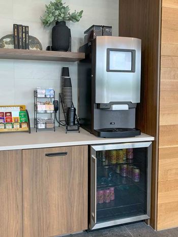 a coffee bar with an espresso machine, a mini fridge with drinks, and tea options in the front lobby