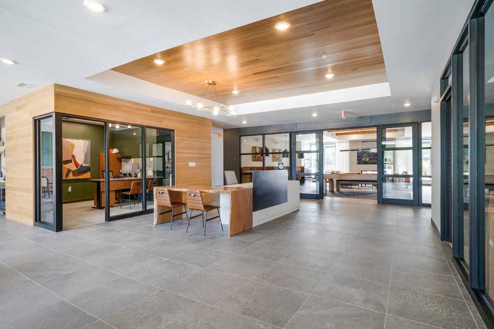 a modern clubhouse lobby with a large free floating stone and wood desk, between two offices with floor to ceiling windows