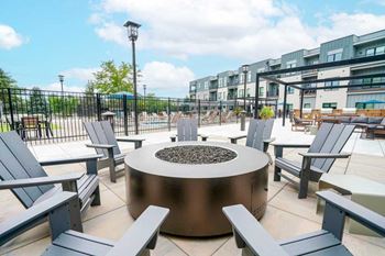 A conversational fire pit with several Adirondack chairs surrounding it.