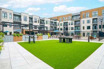 A turfed courtyard with a modern ping pong table and space to play cornhole.
