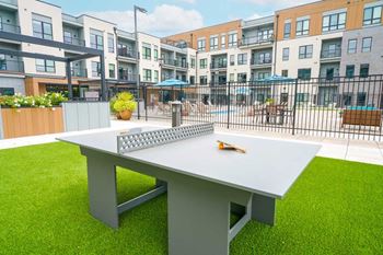 A courtyard with a modern ping pong table on turf grass.