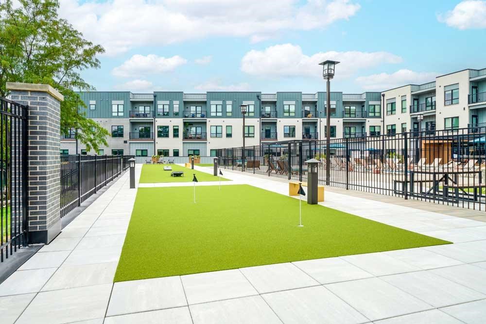 A courtyard with a putting green turf with multiple pins to practice your short game on.