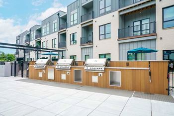 A row of three built-in grilling stations featuring stainless steel gas grills and counters.