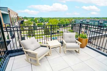 two rocking chairs and a table on a patio with a metal railing overlooking the courtyard below