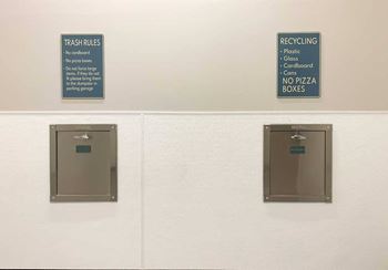 Two stainless steel wall chutes - one for trash and the other for recycling, we respective signs designating what goes into each.