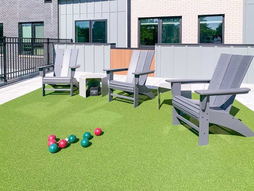 a set of bocce balls in front of Adirondack chairs on a green turf