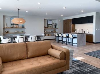 a leather couch in a seating area in front of a dining table and kitchen in the community clubroom