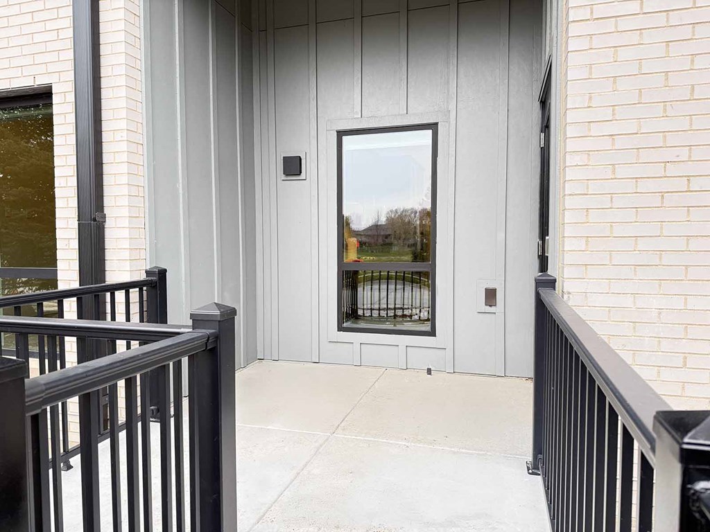 a walk-out patio with black metal railing and a tall window looking into a kitchen