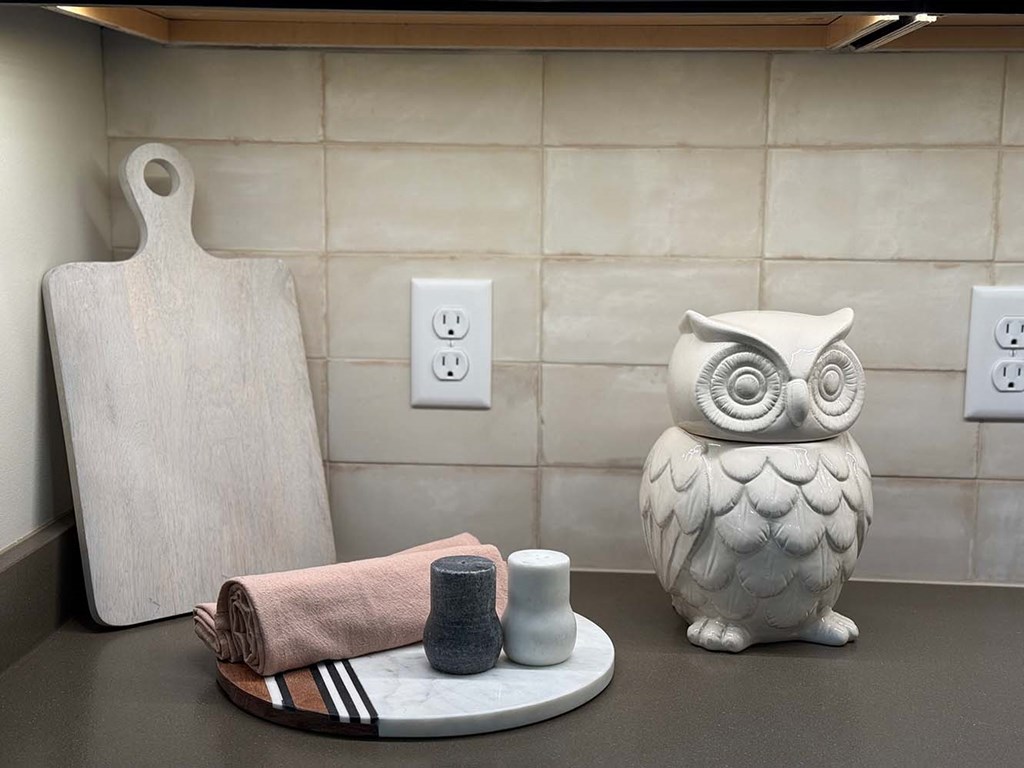 a kitchen countertop decorated with a wooden cutting board, and owl statue, and a serving tray